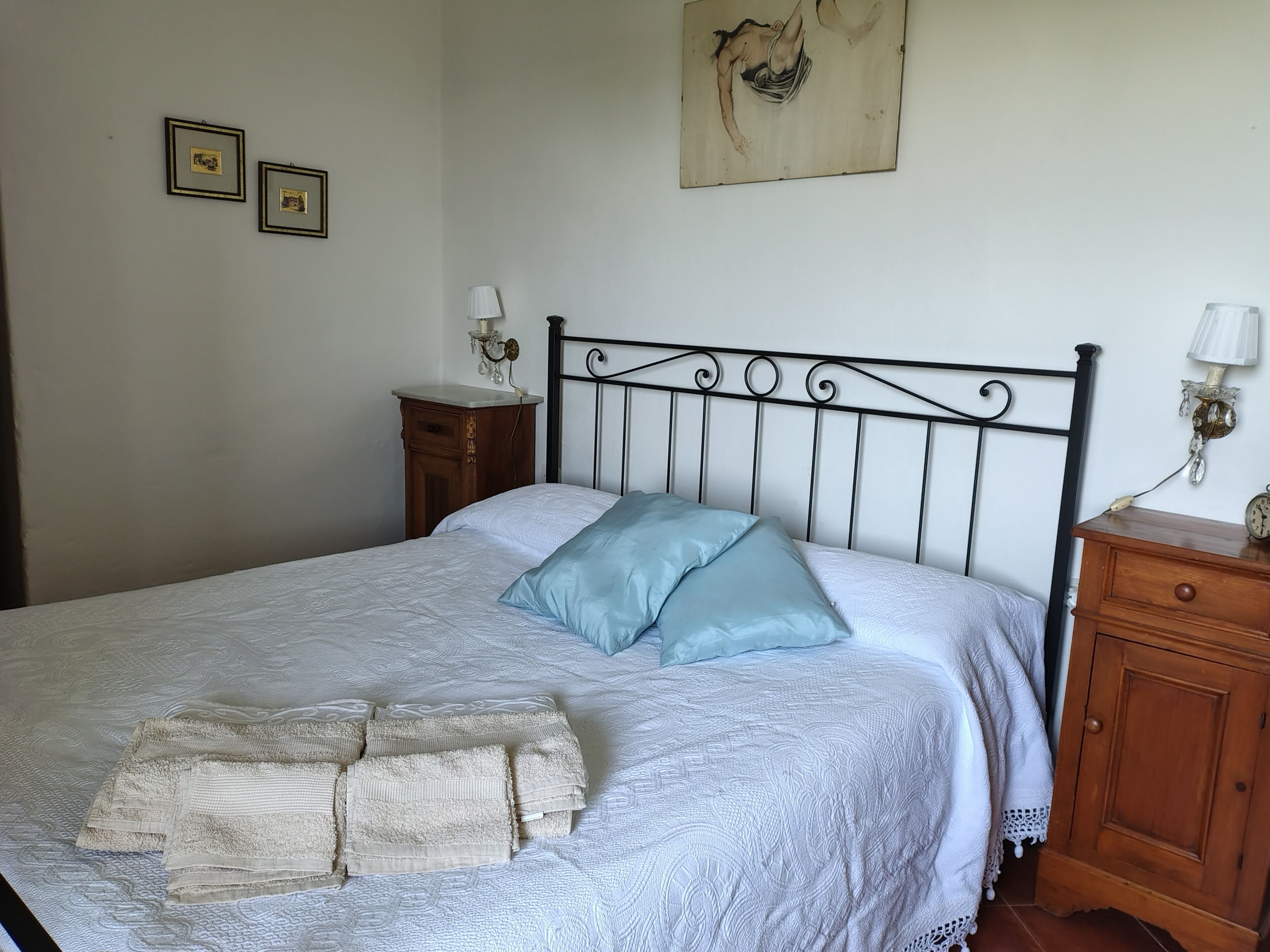 A neatly made bed with a patterned bedspread and two pillows, a wooden nightstand with a lamp, and a wall with framed pictures.