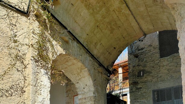 A stone courtyard with an arched structure, cobblestone flooring, and a view of a building with a barred window. - The Bishop's House (Licciana Nardi)