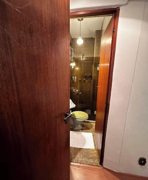Eine Holztür, die zu einem Badezimmer mit Dusche, Toilette und Handtuchhalter führt.