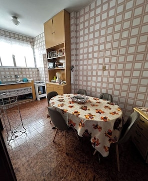A dining area with a round table covered by a floral tablecloth, surrounded by chairs.