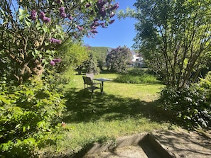 Un giardino con tavolo e sedie, una zona verdeggiante e alberi.