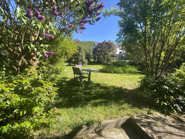 A garden with a table and chairs, a grassy area, and trees.