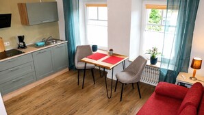 A compact living space with a kitchenette, a dining area with two chairs, a red sofa, and a window with curtains.