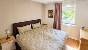 A bedroom with a bed, bedside table, lamp, and a window with curtains.