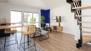 A modern kitchen with a wooden island, bar stools, and a dining table. There is a staircase with a wooden finish and a black metal railing. - Dify Jungle - Villeurbanne (Villeurbanne)