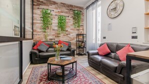 A modern living room with two leather sofas, a coffee table, and a brick wall with hanging plants.