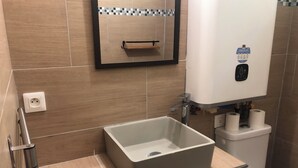 Une salle de bain avec un lavabo rectangulaire, un miroir, un porte-serviettes, des toilettes et un chauffe-eau.