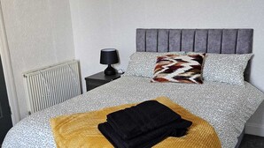 Een net opgemaakt bed met beddengoed met een patroon, een grijs hoofdeinde en twee ingelijste foto's aan de muur.