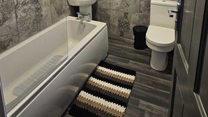 Een badkamer met een badkuip, wastafel, toilet en een raam met uitzicht.