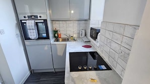 Een compacte keuken met een inbouwoven, magnetron en gasfornuis.