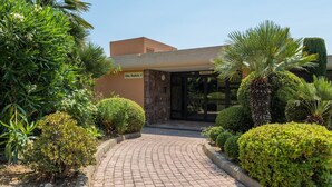 A hotel entrance with a curved brick pathway leading to a glass door. - Apt MEDICIS – Sea View, Terrace & Pool (Mandelieu-la-Napoule)