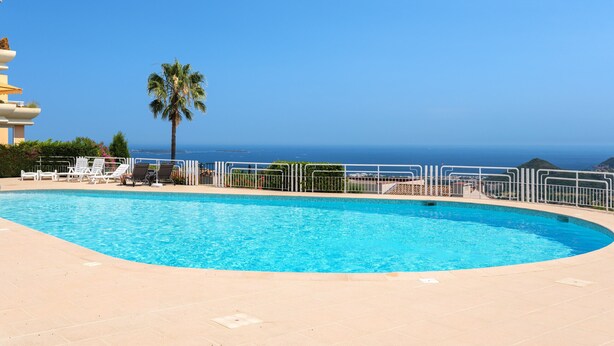 A swimming pool with a view of the ocean, surrounded by a white fence and palm trees. - Apt MEDICIS – Sea View, Terrace & Pool (Mandelieu-la-Napoule)