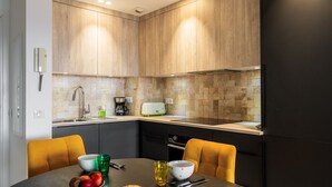 A modern kitchen with wooden cabinets, a countertop, and a dining table with chairs. - Apt MEDICIS – Sea View, Terrace & Pool (Mandelieu-la-Napoule)