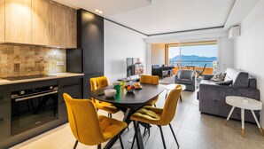 A modern kitchen with a built-in oven, a dining area with yellow chairs, and a grey sofa. - Apt MEDICIS – Sea View, Terrace & Pool (Mandelieu-la-Napoule)