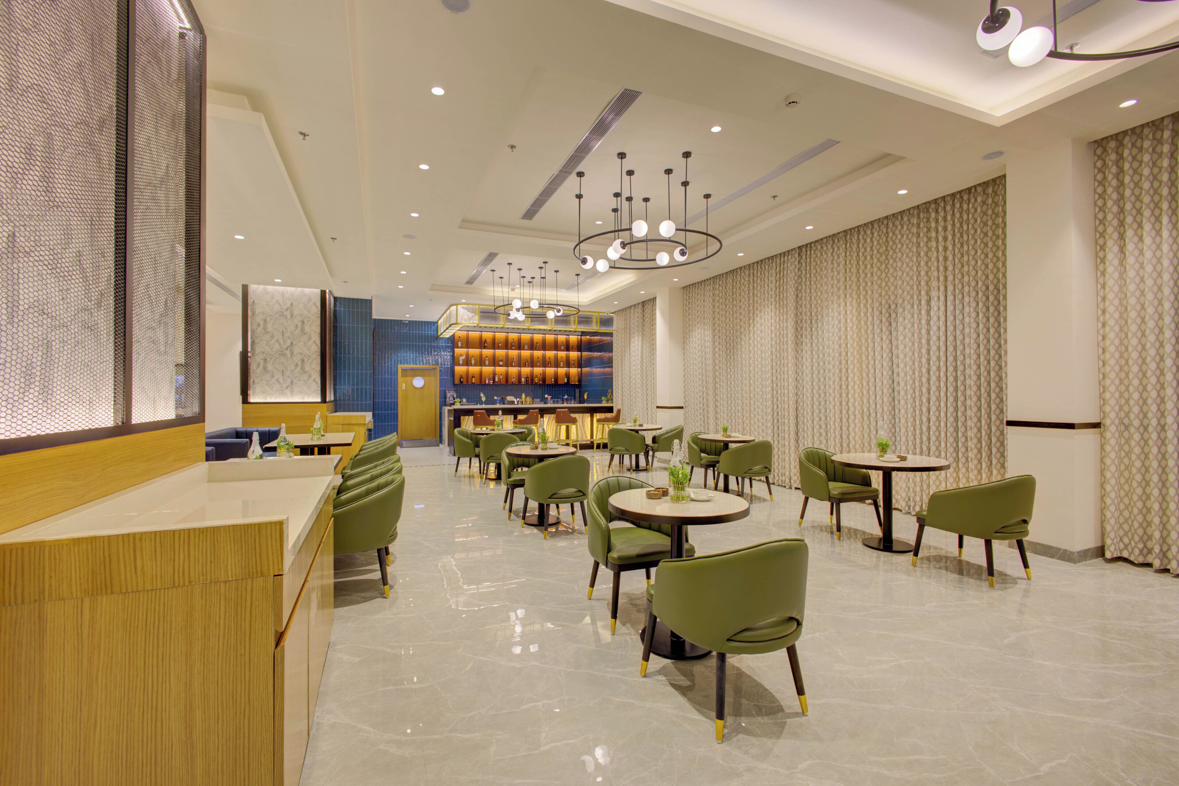 A modern hotel lobby with a reception desk, multiple seating areas, and a bar.