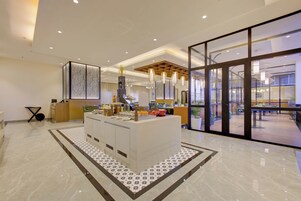 Un moderno vestíbulo de hotel con mostrador de recepción, zona de estar y puertas de cristal grandes que dan a un espacio exterior.