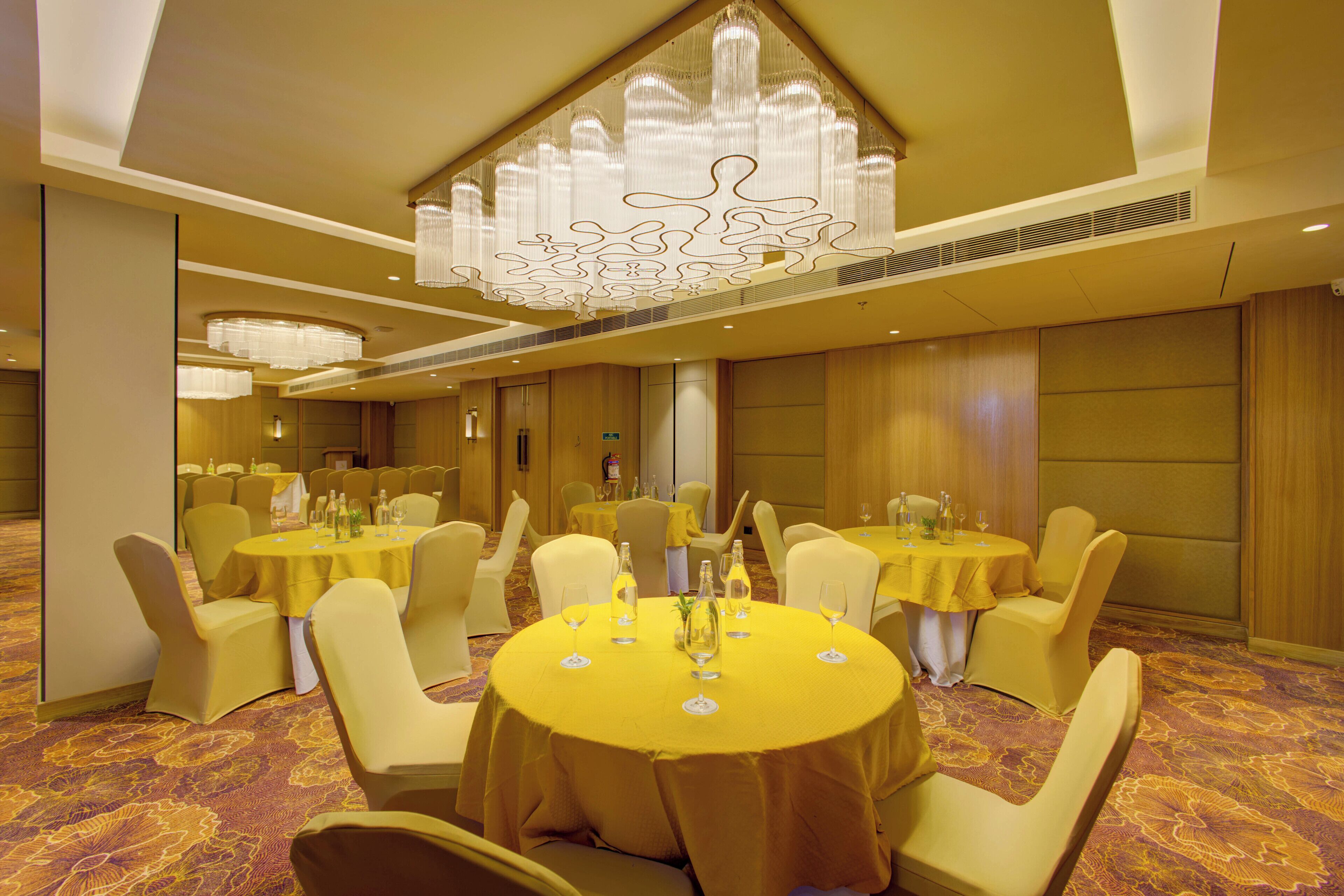 A banquet hall with round tables, yellow tablecloths, and matching chairs.
