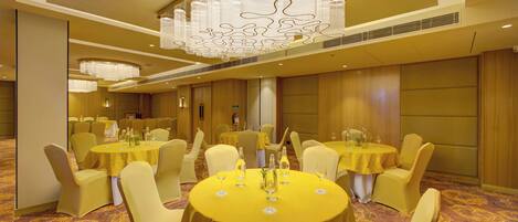 A banquet hall with round tables, yellow tablecloths, and matching chairs.