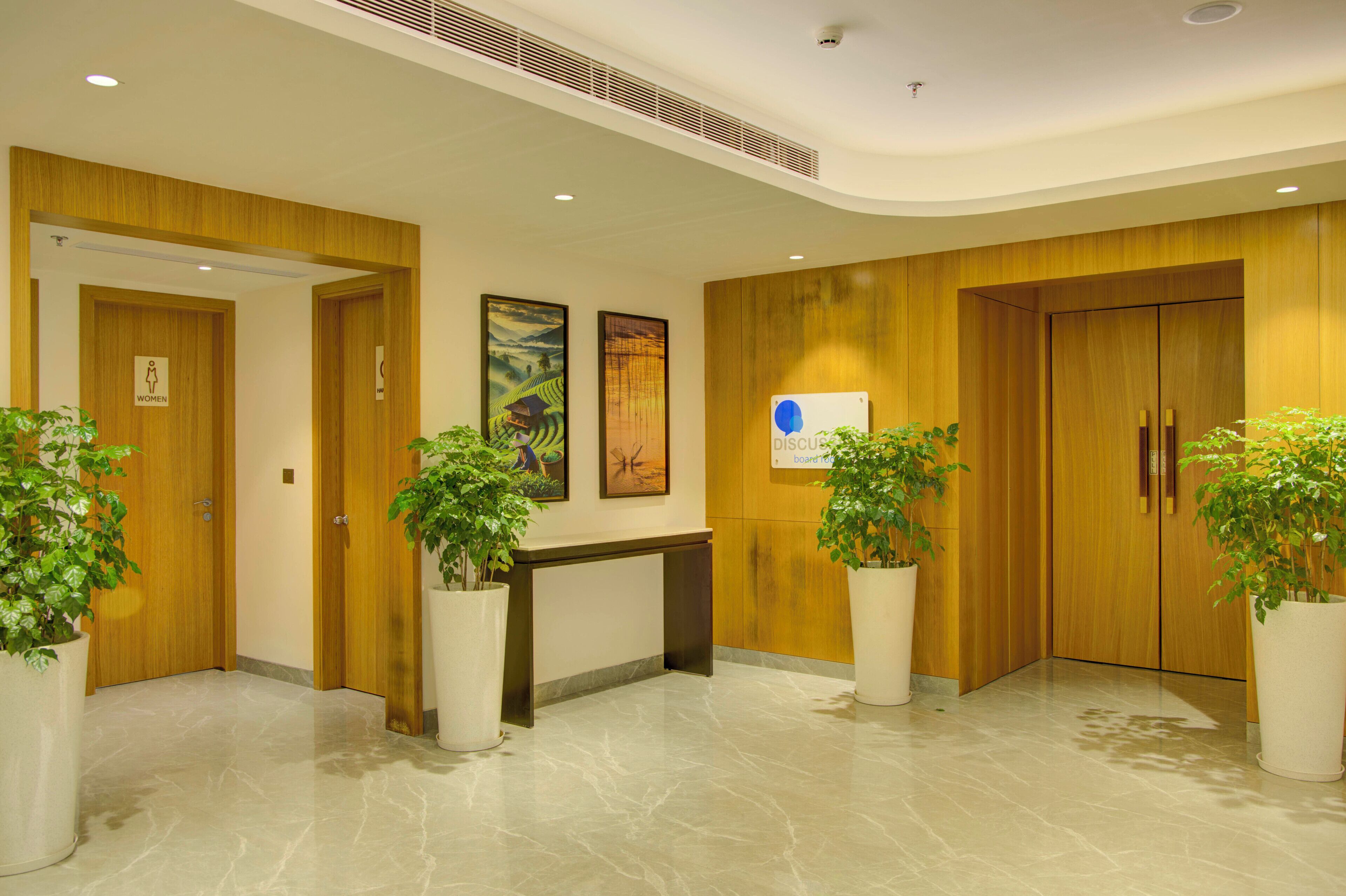 Hall d'albergo con pannelli in legno, una reception e piante in vaso.