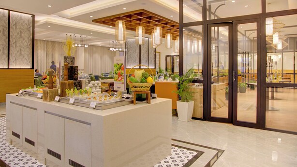 A buffet area with a variety of food items, a seating area with tables and chairs, and a large glass door leading to an outdoor space. - Cygnett Inn Dibrugrah (Dibrugarh)
