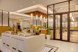 A buffet area with a variety of food items, a seating area with tables and chairs, and a large glass door leading to an outdoor space. - Cygnett Inn Dibrugrah (Dibrugarh)