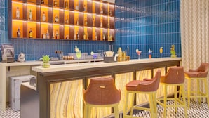 A bar area with a blue tiled backsplash, a variety of bottles, and bar stools. - Cygnett Inn Dibrugrah (Dibrugarh)