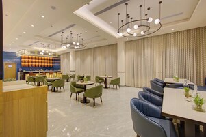 Un moderno vestíbulo de hotel con área de recepción, mesas de comedor y sillas verdes.