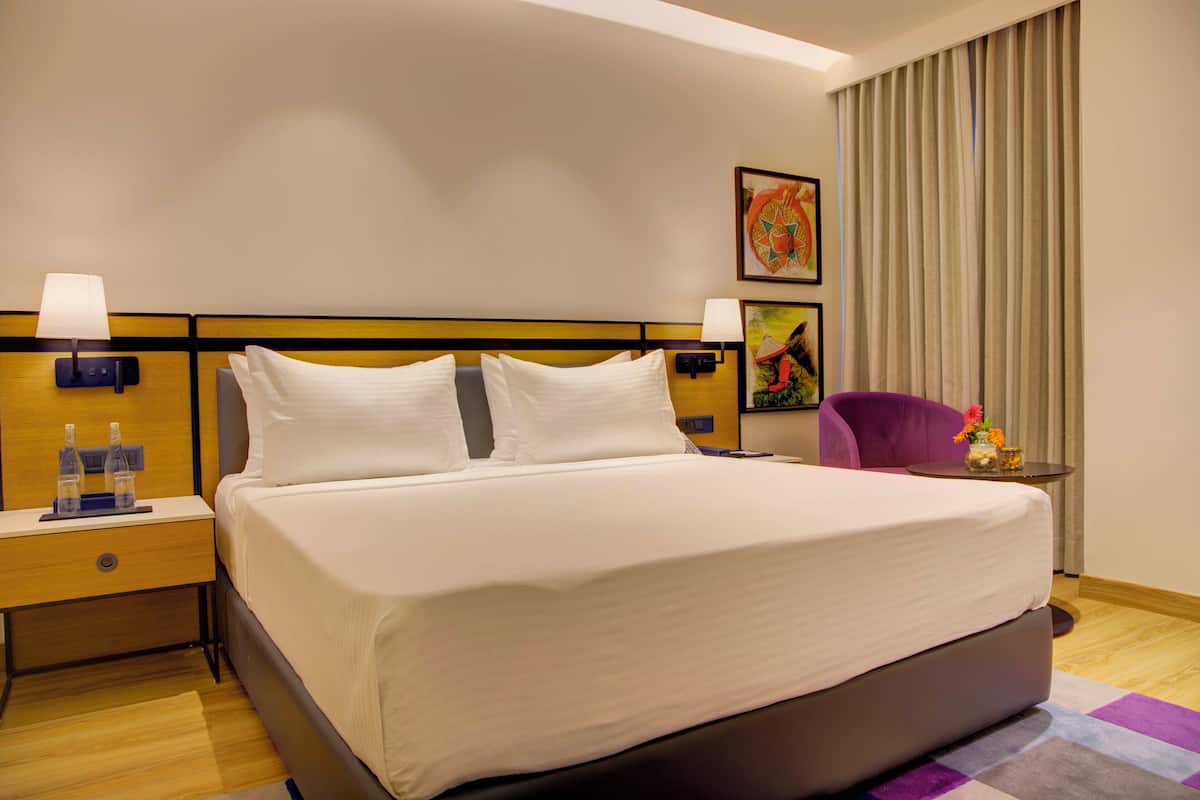 A hotel room with a large bed, two bedside tables with lamps, a small table with a vase of flowers, and a chair.