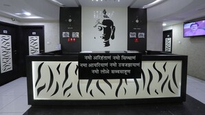 A reception desk with a Buddha mural, a television screen, and a sign with text in a foreign language. - Hotel Paramount Inn (Rajkot)