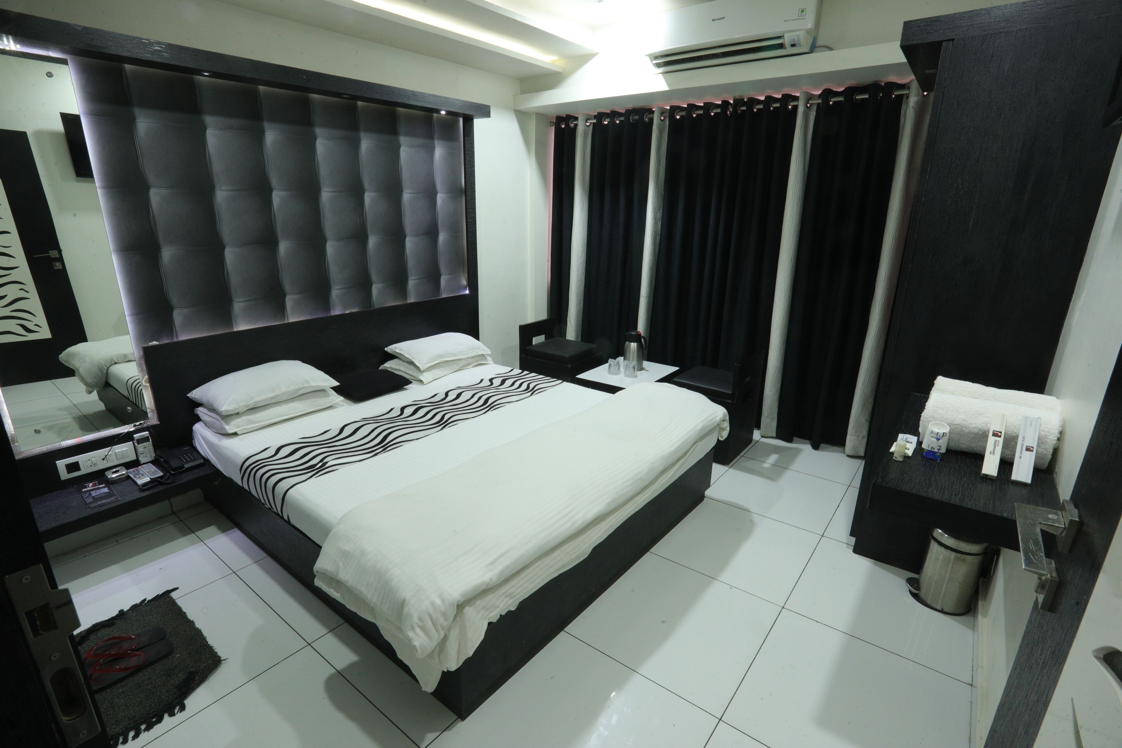 Une chambre d’hôtel avec un grand lit, une table de chevet, un miroir, une commode, une poubelle et une salle de bain comprenant des toilettes et un lavabo.