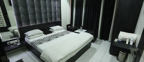 Une chambre d’hôtel avec un grand lit, une table de chevet, un miroir, une commode, une poubelle et une salle de bain comprenant des toilettes et un lavabo.