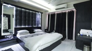 A modern hotel room with a large bed, a bedside table with a lamp, a mirror, and a wardrobe. - Hotel Paramount Inn (Rajkot)