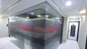 A modern reception area with a glass partition, a digital display, and a tiled floor. - Hotel Paramount Inn (Rajkot)