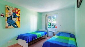 Een kamer met twee bedden, een raam en een kleurrijk schilderij aan de muur.
