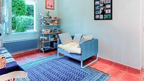 Een kamer met een bed, een blauwe bank, een boekenkast en een raam met uitzicht op groen.