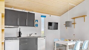 Une cuisine moderne avec des meubles gris, un lave-vaisselle blanc et un coin repas comprenant une table blanche et des chaises bleues.