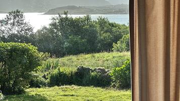 A room with a view of a lake and mountains through a window with a curtain.