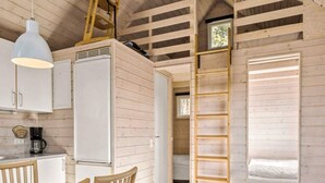 Een kleine kamer met kitchenette, een bed en een houten trap.