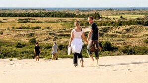 Een zandstrand met mensen die wandelen, een verre uitzicht op de zee en glooiende heuvels op de achtergrond.