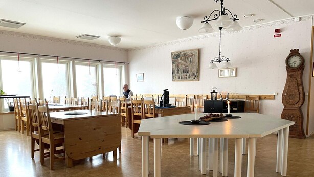 Un'ampia sala da pranzo con tavoli e sedie in legno, una grande orologio a parete e un quadro sopra il camino.