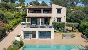 A modern two-story house with a swimming pool, a covered patio, and a view of the surrounding greenery.