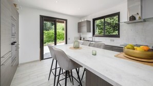 A modern kitchen with a large island, bar stools, and a view of greenery outside.