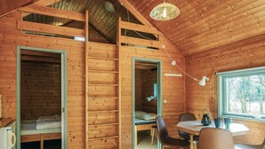 En stuga byggd av trä med ett sovloft, en matplats med stolar och ett stort fönster.