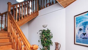 Un escalier en bois avec une rampe, une plante en pot, une petite table avec un vase et un tableau encadré au mur.