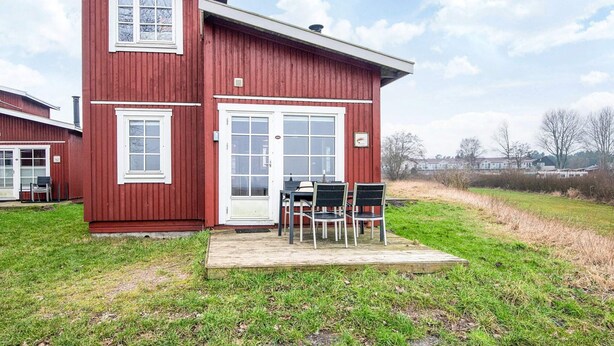 Une maison rouge à deux étages, dotée d’un porche à l’avant et d’une petite table avec des chaises.