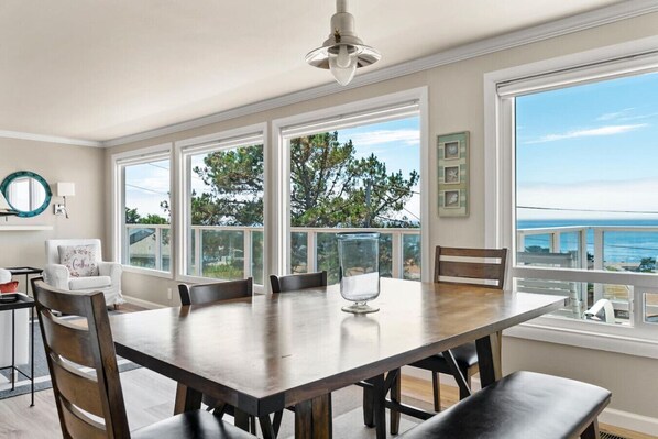 A dining area with a large table, chairs, and a view of the ocean.