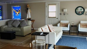 Ein Wohnzimmer mit einer Couch, einem weißen Sessel, einem Couchtisch, einem Bücherregal, einem Buntglasfenster und einer Tür mit Fenster.