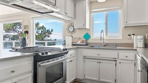 Eine moderne Küche mit weißen Schränken, einem Edelstahlherd und einem Fenster mit Meerblick.