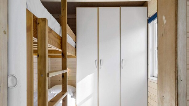 Un lit superposé avec une armoire blanche et une fenêtre.