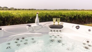 Jacuzzi con una botella de agua mineral y dos vasos, rodeado de exuberante vegetación.